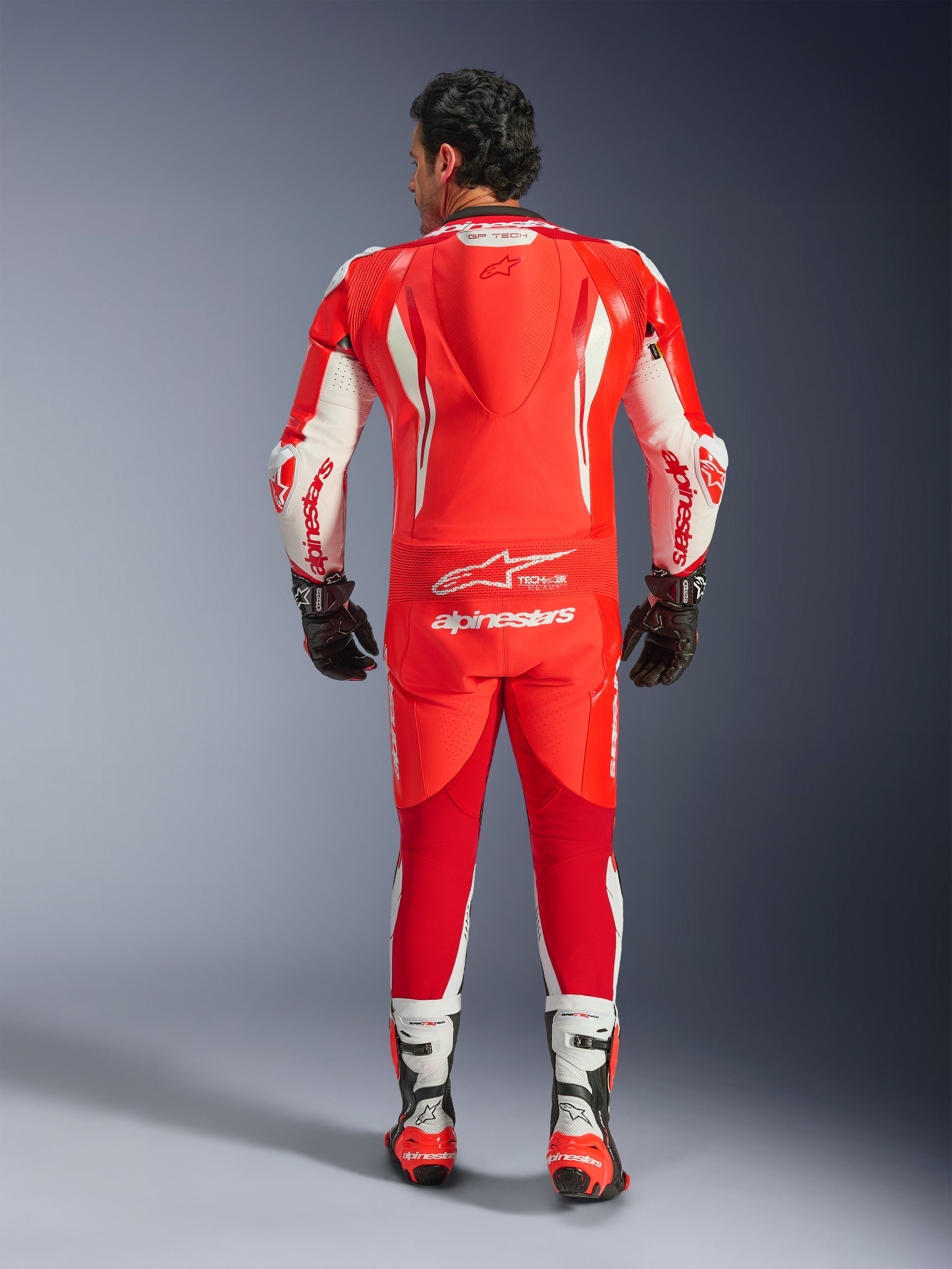 Alpinestars GP Tech V5 One Piece Leather Suit, tuta da corsa per moto, rosso fluo, rosso acceso e bianco, vista posteriore con gobba aerodinamica e logo Alpinestars bianco, indossata con guanti e stivali da corsa bianchi e neri