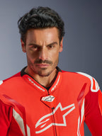 Alpinestars GP Tech V5 One Piece Leather Suit, tuta da corsa per motociclismo, rosso fluo, rosso brillante e bianco, ritratto ravvicinato di un pilota, petto in pelle traforata con logo Alpinestars bianco, colletto da corsa ad alte prestazioni e design aerodinamico.
