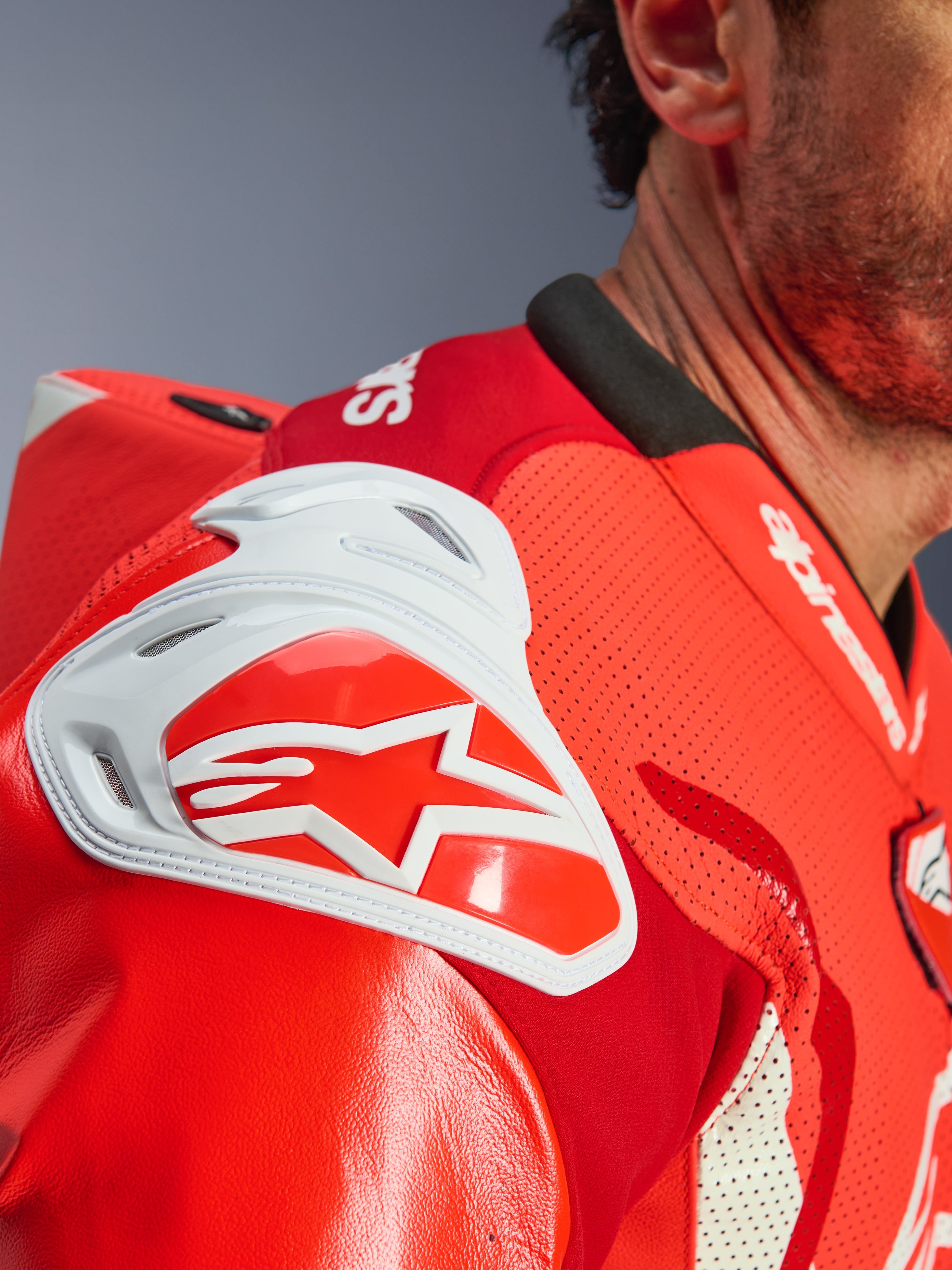 Tuta in pelle Alpinestars GP Tech V5 1PC, primo piano della zona della spalla in Rosso Fluo e Rosso Vivo, con protezione dagli impatti GP DFS bianca, logo a stella rosso e pelle traforata per la ventilazione.