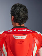 Primo piano della parte superiore della schiena e del collo della tuta in pelle GP Tech V5, Red Fluo e Bright Red, con scritta Alpinestars bianca sul colletto e logo GP TECH sulla gobba aerodinamica, indossata da un pilota.