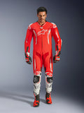 Alpinestars GP Tech V5, tuta professionale da corsa in pelle monopezzo, rosso fluo e rosso brillante con accenti bianchi, indossata da un pilota con stivali e guanti coordinati, con gobba aerodinamica, costruzione in pelle premium e protezioni avanzate per prestazioni in pista