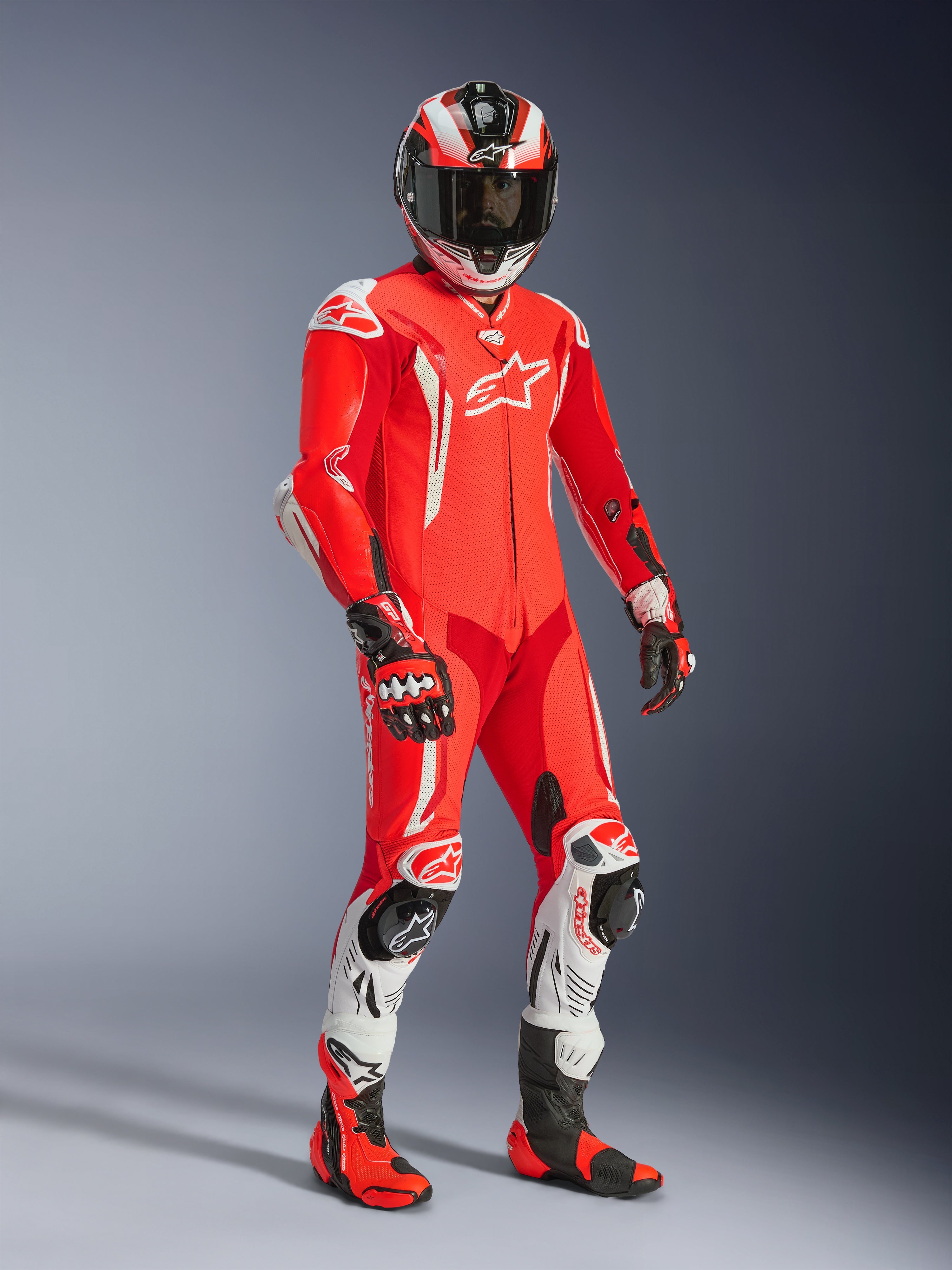 Pilota di moto con tuta in pelle intera Alpinestars GP Tech V5, Rosso Fluo e Rosso Brillante con dettagli bianchi, completa di casco, guanti e stivali da corsa abbinati, abbigliamento professionale da pista con pelle traforata e slider protettivi