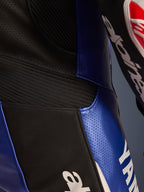 Dettaglio ravvicinato della tuta in pelle intera Alpinestars Yamaha GP-R7, blu metallizzato e nero, pannelli in pelle traforata per la ventilazione, inserti elastici a soffietto neri per la flessibilità e branding Yamaha bianco, costruzione in pelle bovina di qualità professionale.