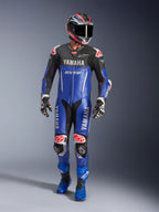 Alpinestars Yamaha GP-R7 One Piece Leather Suit, tuta da corsa in pelle monopezzo, blu metallizzato e nero con dettagli rossi e bianchi, loghi Yamaha e GYTR, indossata con casco, guanti da corsa e stivali blu abbinati, equipaggiamento professionale ad alte prestazioni