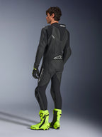 Tuta in pelle Alpinestars GP Force V2, tuta da moto racing monopezzo nera, vista posteriore che mostra la gobba aerodinamica e la pelle traforata, indossata con stivali da corsa giallo neon e guanti neri, attrezzatura professionale pronta per la pista
