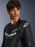 Primo piano di un uomo che indossa la tuta in pelle Alpinestars GP Force V2 in nero, caratterizzata da una struttura in pelle traforata, logo Alpinestars con scritta 'RACING AHEAD' sul petto e logo a stella bianco sugli slider delle spalle.