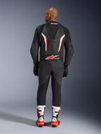 Vista posteriore di un modello che indossa la tuta in pelle intera Alpinestars GP Force V2 in Nero Bianco Rosso Fluo, mettendo in evidenza la gobba aerodinamica e il marchio Tech-Air Ready, abbinata a stivali da corsa professionali bianchi e rossi e guanti neri.