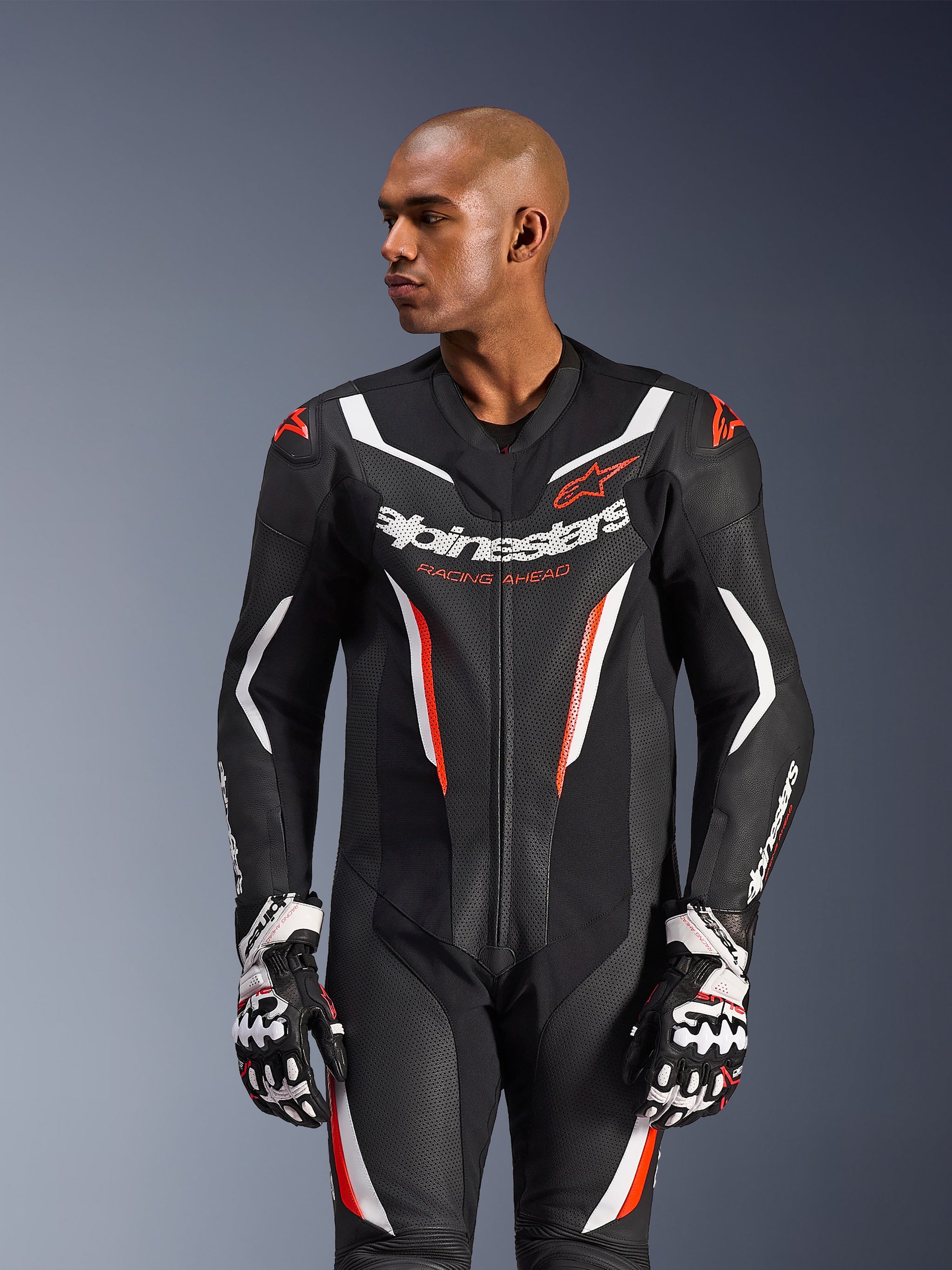 Alpinestars GP Force V2 Leather Suit - 1Piece, tuta racing da moto, nero, bianco e rosso fluo, con pannelli in pelle traforata, logo evidente sul petto con scritta 'Racing Ahead' e design protettivo ergonomico, indossata con guanti racing coordinati