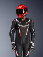 Pilota di moto che indossa la tuta in pelle intera Alpinestars GP Force V2 in nero, bianco e rosso fluo, casco da corsa e guanti rossi coordinati, dotata di pannelli in pelle traforata e branding audace, equipaggiamento racing ad alte prestazioni