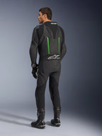 Tuta in pelle Alpinestars GP Force V2, tuta da moto intera, nero con dettagli verdi, vista posteriore che mostra la gobba aerodinamica e il logo bianco sul pannello elastico a fisarmonica, abbinata a stivali e guanti da corsa neri.