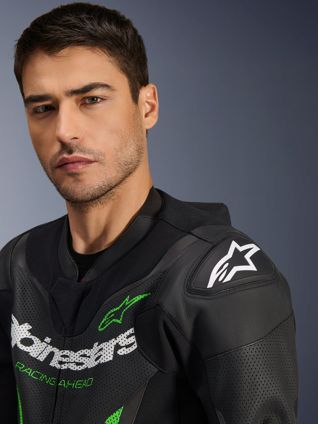 Alpinestars GP Force V2 Leather Suit - 1Piece, tuta in pelle da moto, nero e verde, primo piano di un modello maschile che indossa la tuta da corsa, con loghi bianchi e verdi, pannelli in pelle traforata e protezione per le spalle DFS Lite con logo a stella bianco