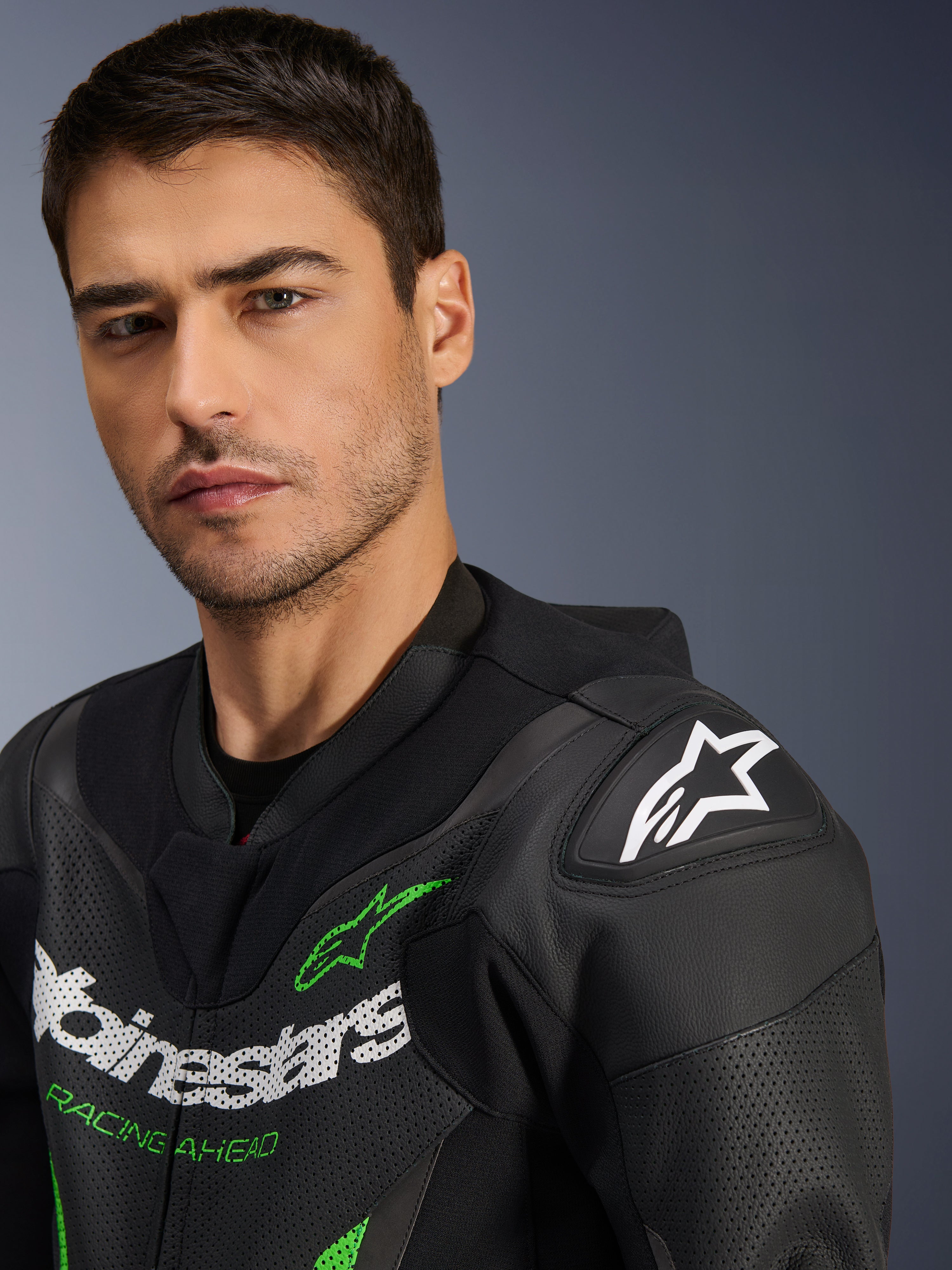 Alpinestars GP Force V2 Leather Suit - 1Piece, tuta in pelle da moto, nero e verde, primo piano di un modello maschile che indossa la tuta da corsa, con loghi bianchi e verdi, pannelli in pelle traforata e protezione per le spalle DFS Lite con logo a stella bianco