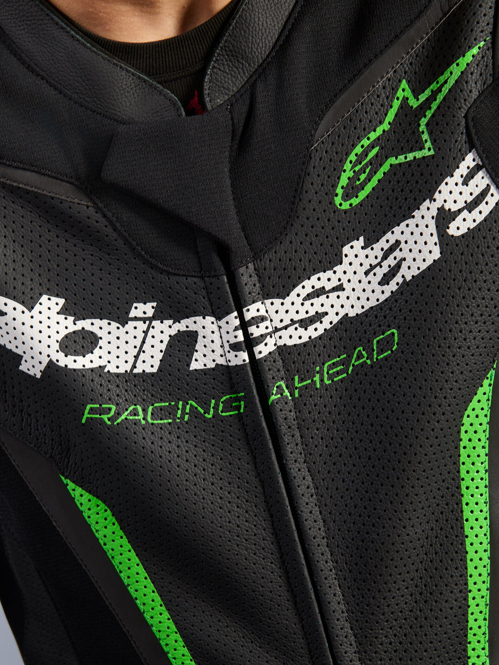 Alpinestars GP Force V2 Leather Suit - 1 pezzo, primo piano della zona del torace, pelle nera traforata con marchio Alpinestars bianco, scritta 'RACING AHEAD' verde e accenti verdi