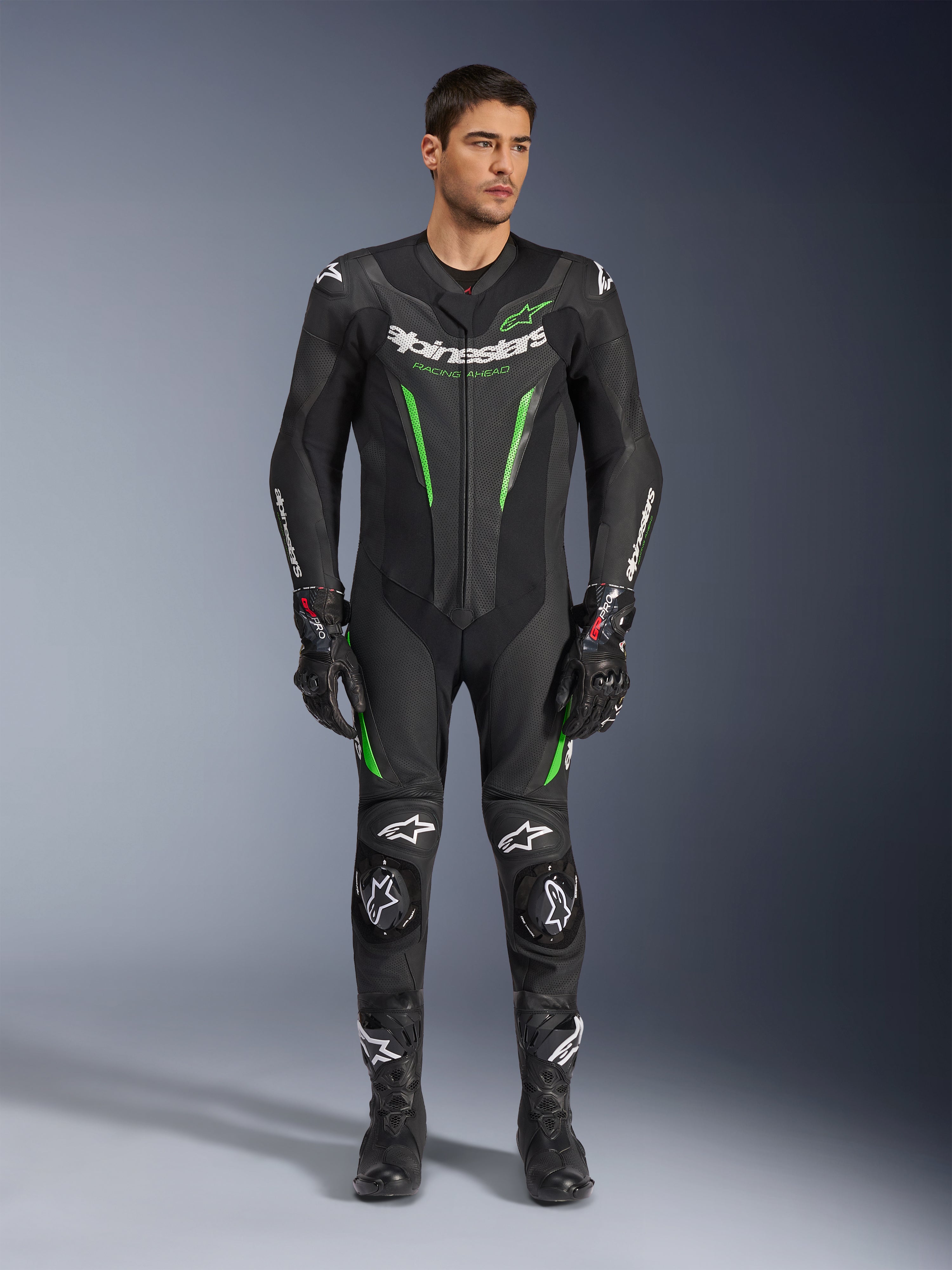 Alpinestars GP Force V2 Leather Suit - 1 pezzo, tuta da corsa motociclistica intera, nero e verde, vista frontale di un modello che indossa la tuta con logo bianco sul petto e accenti verde neon, con pelle traforata e slider esterni sulle spalle, abbinata a guanti e stivali da corsa neri