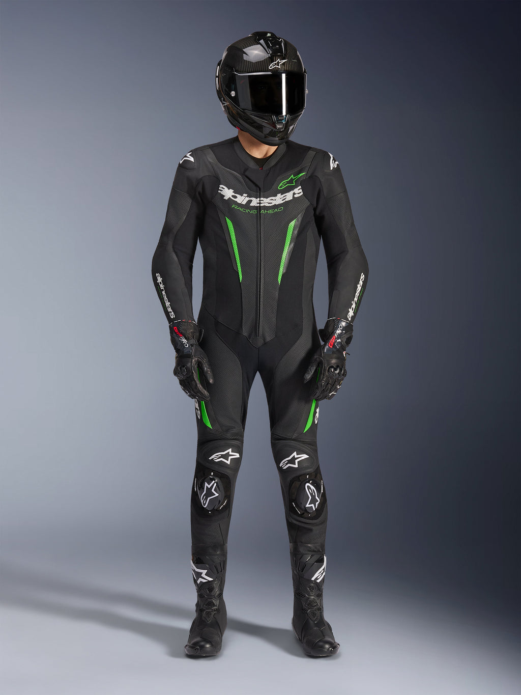 Pilota di moto che indossa la tuta in pelle Alpinestars GP Force V2 - 1 Pezzo in nero e verde, abbinata a un casco in fibra di carbonio e guanti racing, con pannelli in pelle perforata e loghi Alpinestars bianchi, equipaggiamento professionale da pista e guida sportiva