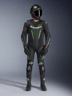 Pilota di moto che indossa la tuta in pelle Alpinestars GP Force V2 - 1 Pezzo in nero e verde, abbinata a un casco in fibra di carbonio e guanti racing, con pannelli in pelle perforata e loghi Alpinestars bianchi, equipaggiamento professionale da pista e guida sportiva