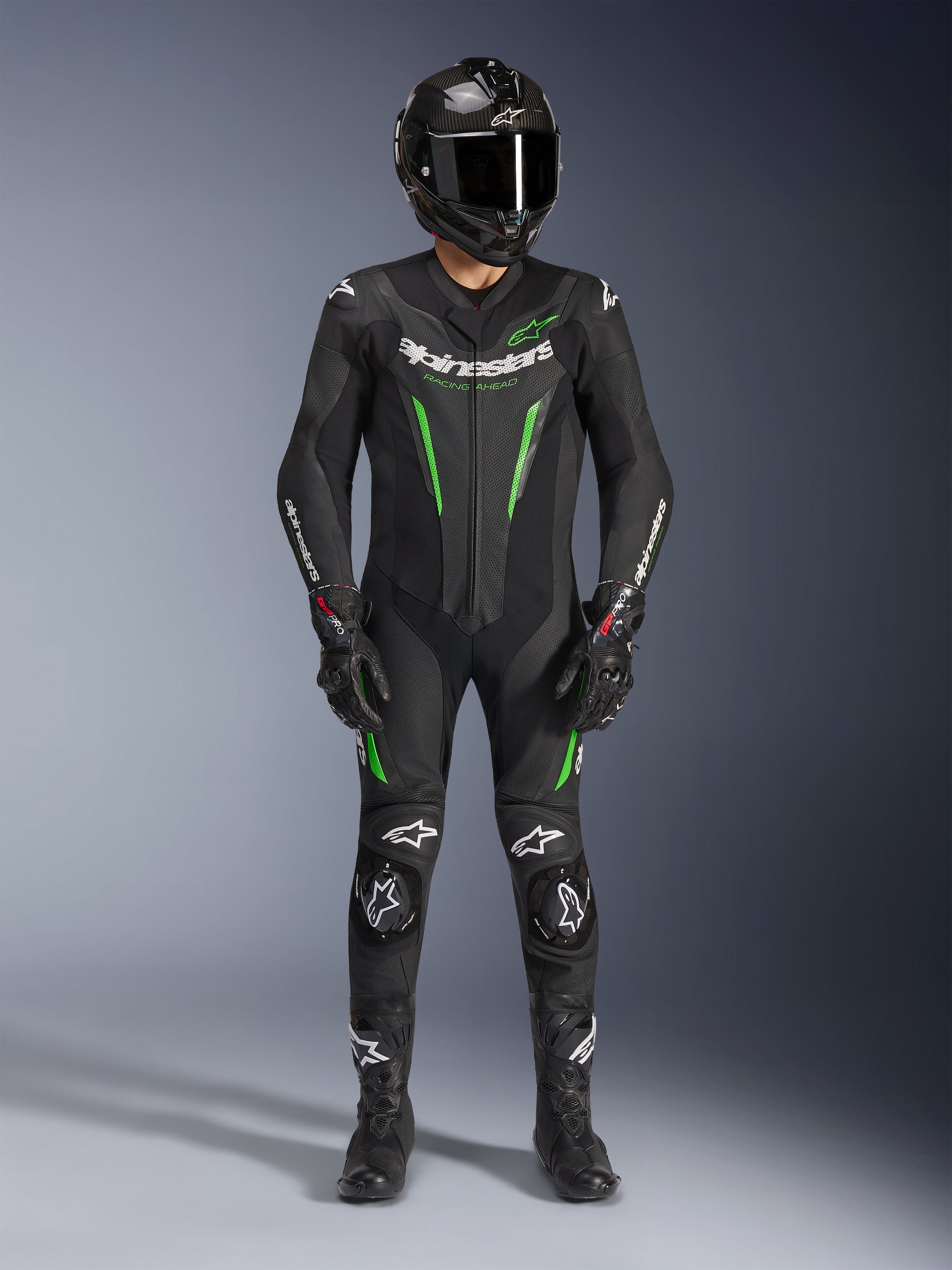 Pilota di moto che indossa la tuta in pelle Alpinestars GP Force V2 - 1 Pezzo in nero e verde, abbinata a un casco in fibra di carbonio e guanti racing, con pannelli in pelle perforata e loghi Alpinestars bianchi, equipaggiamento professionale da pista e guida sportiva