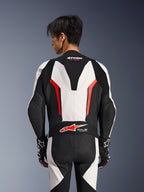 Alpinestars GP Force V2 Leather Suit 1 Pezzo, bianco, nero e rosso fluo, vista posteriore su modello maschile, con gobba aerodinamica, pannelli in pelle traforata e logo Tech-Air Ready sulla parte bassa della schiena, abbigliamento racing professionale con guanti neri e bianchi