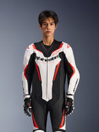 Tuta in pelle Alpinestars GP Force V2 - Monopezzo, bianco, nero e rosso fluo, indossata da un modello, con pannelli in pelle traforata e logo Alpinestars sul petto, coordinata con guanti da corsa bianchi e neri, progettata per la pista e la guida sportiva