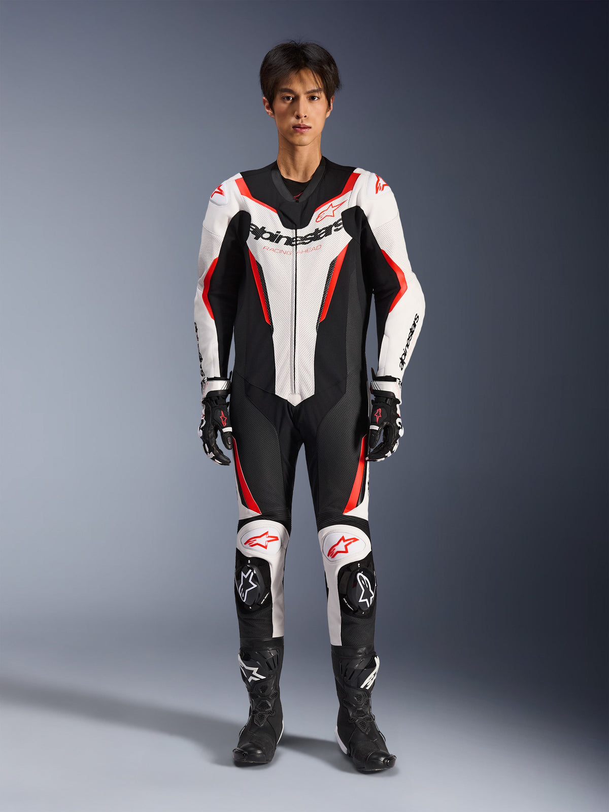 Alpinestars GP Force V2 Leather Suit - 1Piece, Bianco Nero Rosso Fluo, tuta da moto intera in pelle, vista frontale su modello, con pannelli traforati e accenti rossi, logo Alpinestars prominente sul petto, abbinata a stivali e guanti da corsa professionali