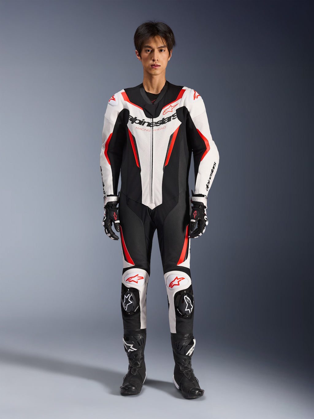 Alpinestars GP Force V2 Leather Suit - 1Piece, Bianco Nero Rosso Fluo, tuta da moto intera in pelle, vista frontale su modello, con pannelli traforati e accenti rossi, logo Alpinestars prominente sul petto, abbinata a stivali e guanti da corsa professionali