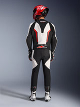 Tuta in pelle Alpinestars GP Force V2 - Monopezzo, Bianco Nero Rosso Fluo, vista posteriore che evidenzia la gobba aerodinamica e il marchio Tech-Air Ready, indossata con casco da corsa rosso e stivali bianchi e neri, tuta in pelle per prestazioni in pista.