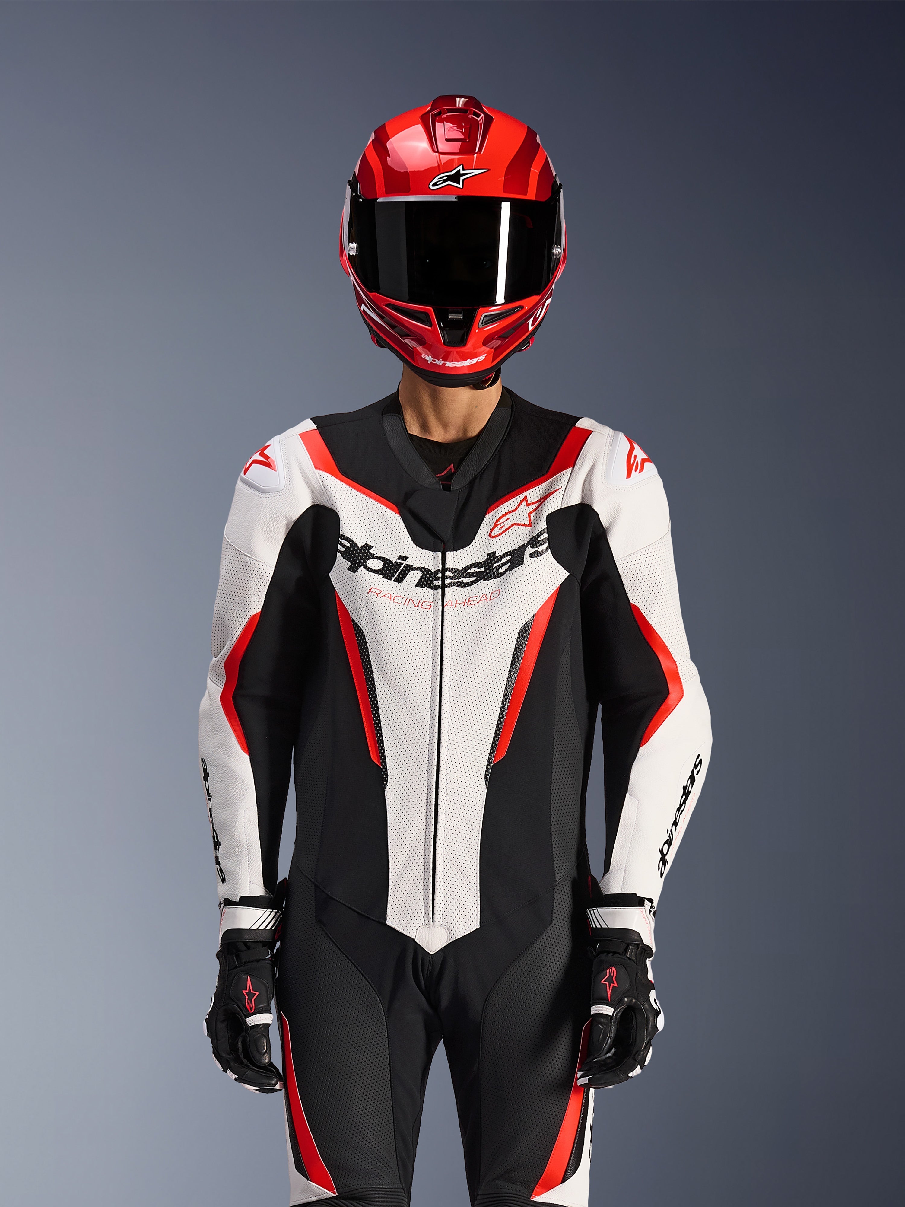 Alpinestars GP Force V2 Leather Suit - Monopezzo, Bianco Nero Rosso Fluo, indossata con casco integrale rosso e guanti da corsa neri, con pannelli in pelle traforata e logo Alpinestars sul petto, abbigliamento professionale per competizioni motociclistiche