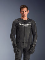 Tuta in pelle Alpinestars GP Force V2 2 pezzi, nero, indossata da un modello, con pannelli in pelle traforata e logo bianco 'Alpinestars Racing Ahead' sul petto, abbinata a guanti neri, abbigliamento professionale per guida sportiva