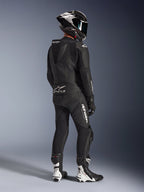 Alpinestars GP Force V2 2-Piece Leather Suit, tuta in pelle a due pezzi, nera, vista posteriore di un pilota con attrezzatura da corsa completa, gobba aerodinamica, loghi bianchi e pelle traforata, abbinata a casco in fibra di carbonio e stivali racing neri e bianchi