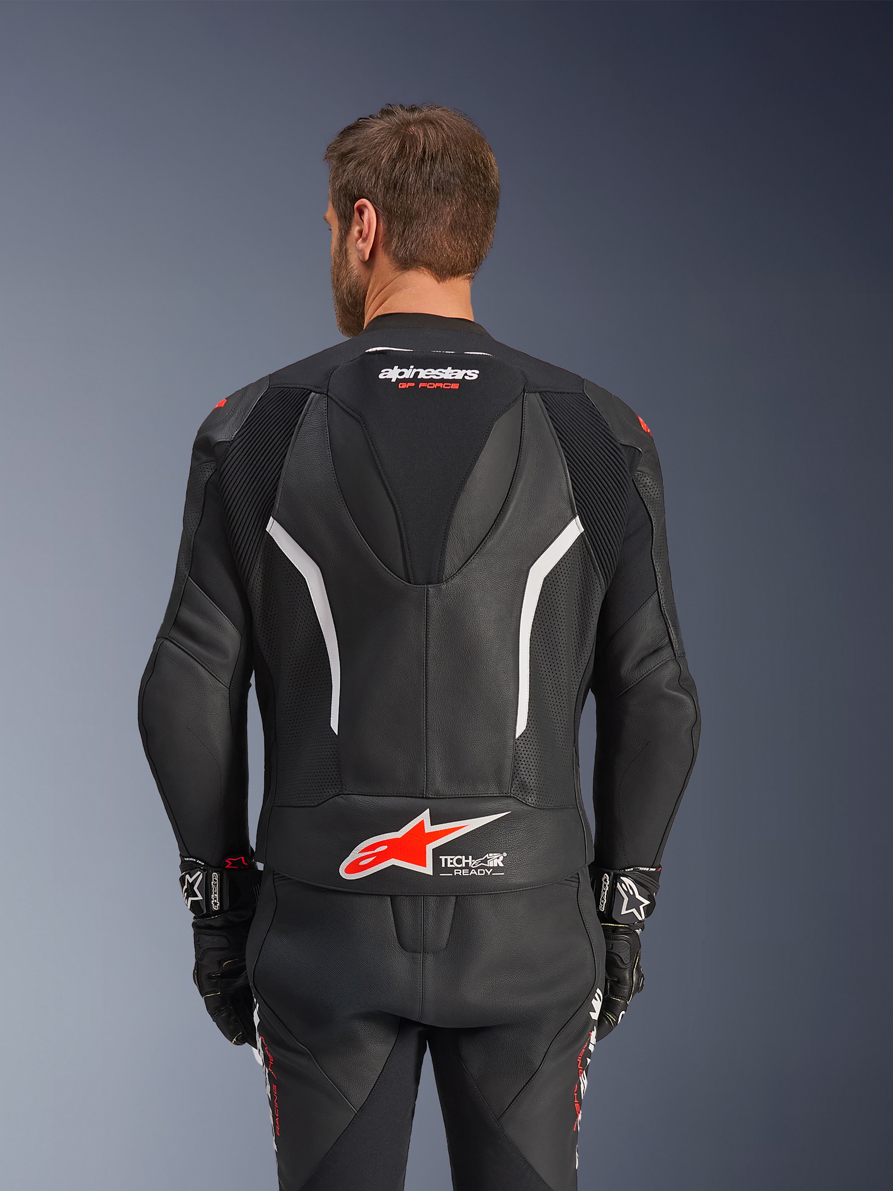 Alpinestars GP Force V2 Leather Suit - 2 pezzi, nero bianco e rosso fluo, vista posteriore della giacca in pelle, con logo Tech-Air Ready, accenti bianchi, pannelli in pelle traforata e inserti elasticizzati a fisarmonica per la mobilità.