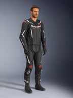 Tuta in pelle Alpinestars GP Force V2 2 pezzi, nero, bianco e rosso fluo, indossata da un modello con stivali e guanti racing neri, con pannelli in pelle traforata, accenti aerodinamici bianchi e loghi rosso fluo su spalle e ginocchia, abbigliamento professionale da moto
