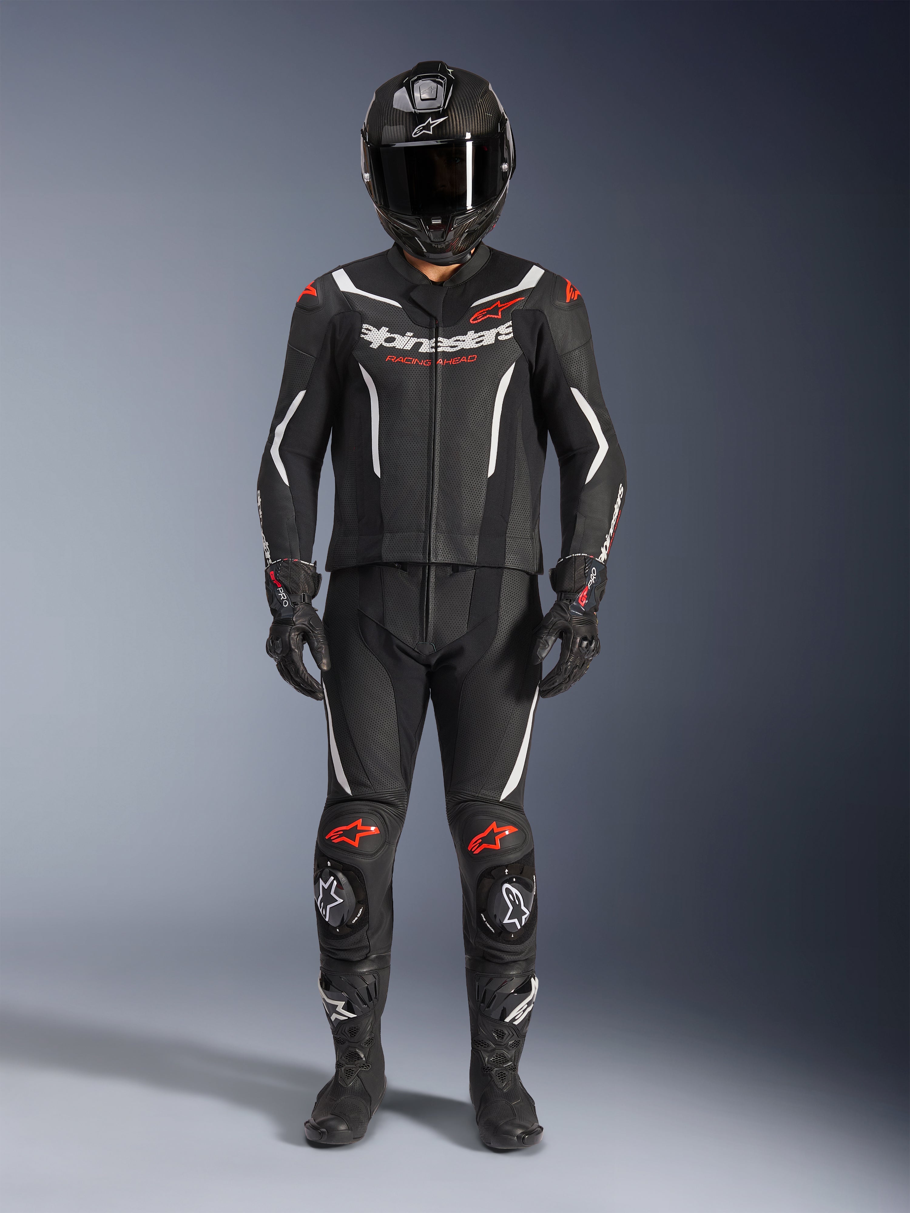 Alpinestars GP Force V2 Leather Suit 2 pezzi, tuta racing da moto, nero, bianco e rosso fluo, con logo Alpinestars bianco sul petto e accenti rossi su spalle e ginocchia, indossata con casco integrale nero, guanti neri e stivali neri per un set completo di equipaggiamento ad alte prestazioni