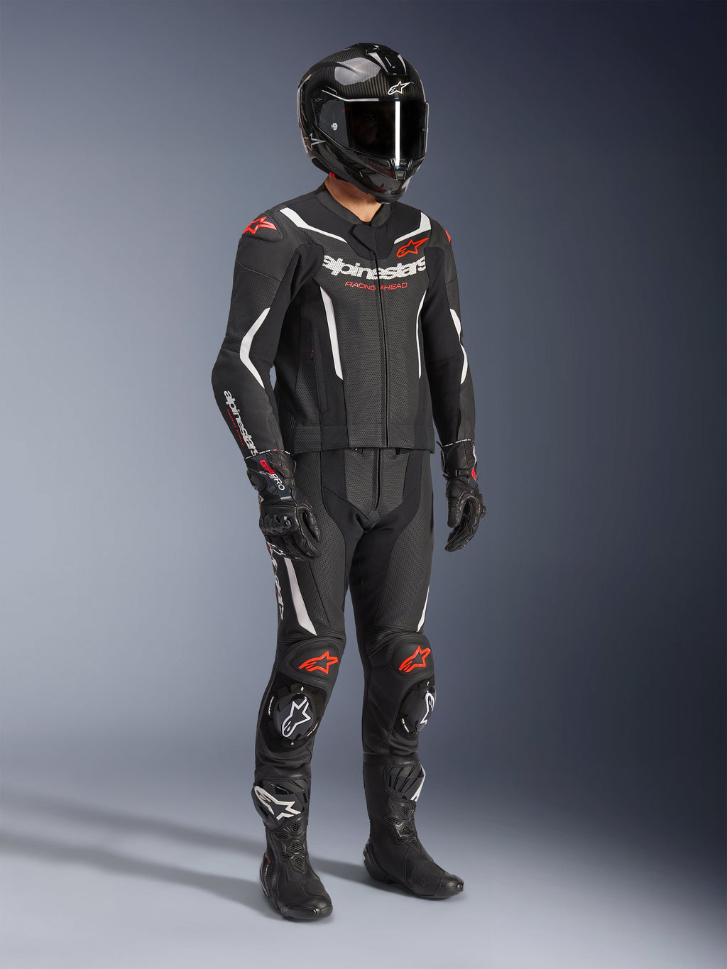 Tuta in pelle Alpinestars GP Force V2 2 pezzi, nero, bianco e rosso fluo, abbigliamento completo da moto racing con casco in fibra di carbonio, guanti racing e stivali, costruzione in pelle con pannelli traforati e gobba aerodinamica.