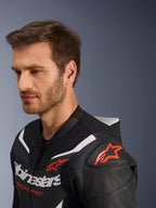 Tuta in pelle Alpinestars GP Force V2 2-Pezzi, primo piano della giacca indossata da un modello, nero, bianco e rosso fluo, caratterizzata da pelle traforata, logo a stella rosso sulla spalla, gobba aerodinamica e marchio Alpinestars sul petto, abbigliamento professionale per motociclismo racing
