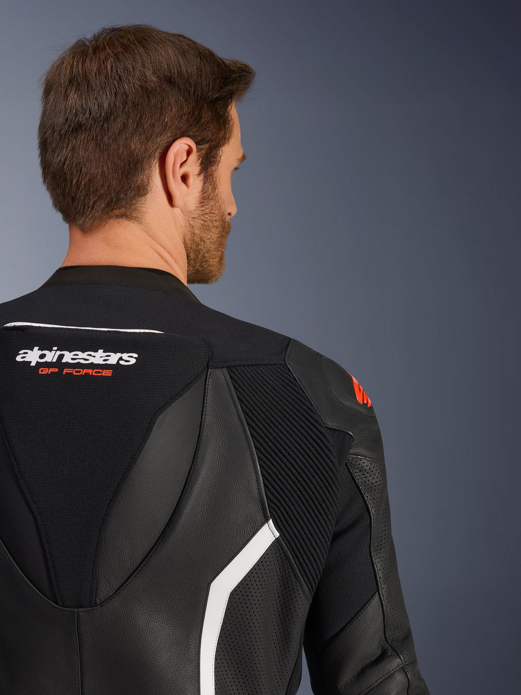 Tuta in pelle Alpinestars GP Force V2 2 pezzi, primo piano della parte superiore della schiena e della spalla su un modello maschile, pelle nera con accenti bianchi e rossi, marchio GP Force, con pannelli traforati e zone elasticizzate a fisarmonica per corse motociclistiche