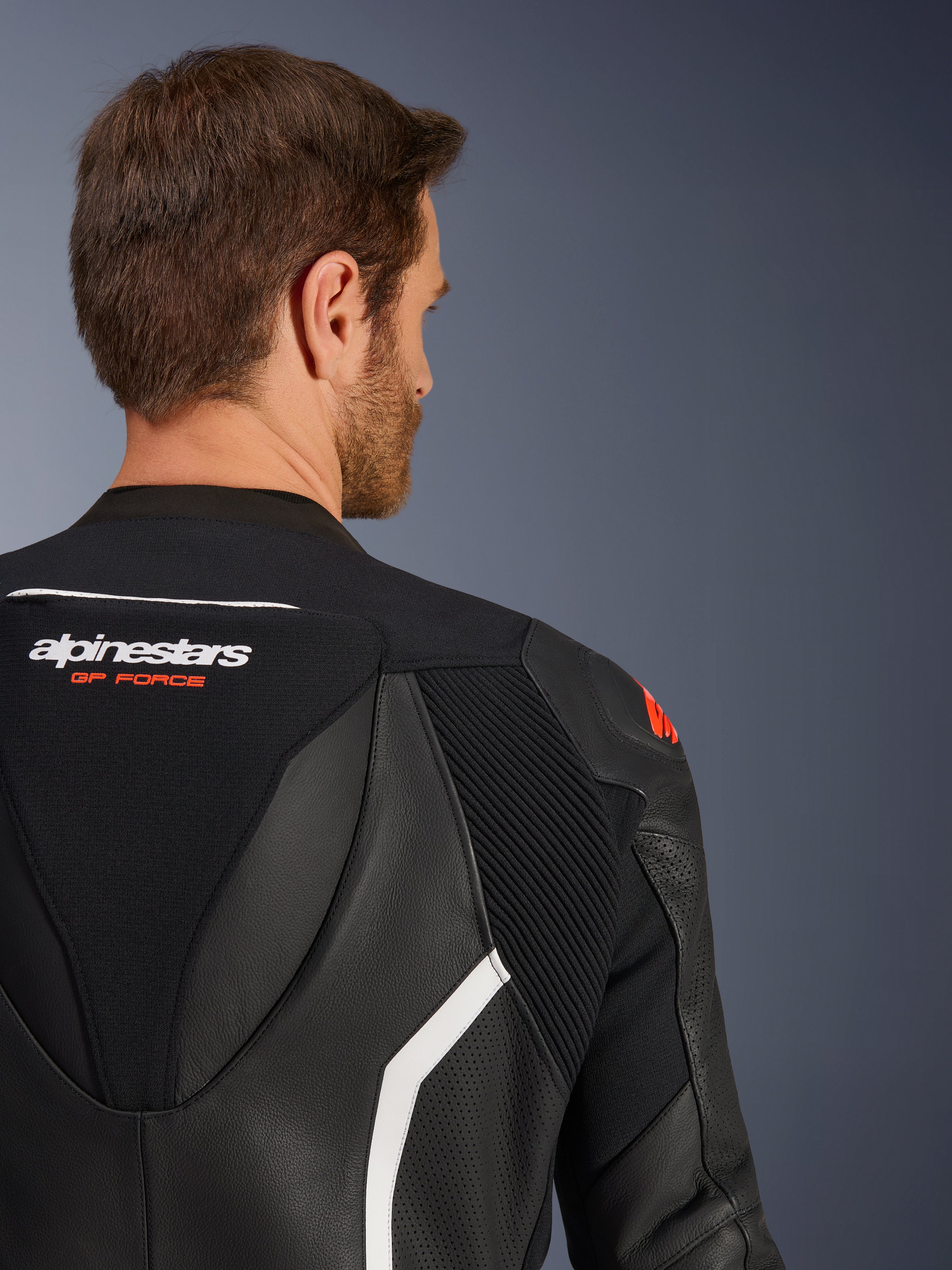 Tuta in pelle Alpinestars GP Force V2 2 pezzi, primo piano della parte superiore della schiena e della spalla su un modello maschile, pelle nera con accenti bianchi e rossi, marchio GP Force, con pannelli traforati e zone elasticizzate a fisarmonica per corse motociclistiche