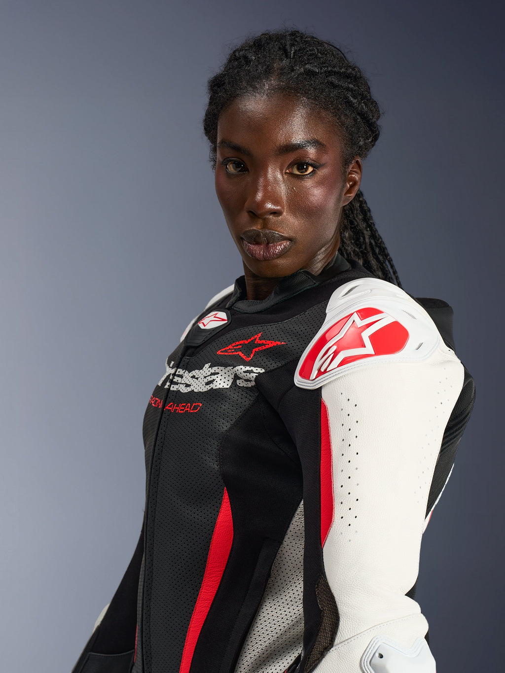 Motociclista che indossa la tuta in pelle Alpinestars Stella GP-R7 2 pezzi, nero, bianco e rosso fluo, con protezioni per le spalle bianche e logo a stella rosso, petto in pelle traforata e design professionale ispirato alle corse