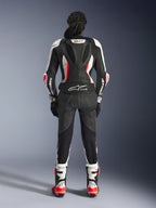 Vista posteriore della tuta in pelle Alpinestars Stella GP-R7 2 Pezzi, nero, bianco e rosso fluo, con gobba aerodinamica con branding GP-R7 e logo Tech-Air Ready, indossata con stivali e guanti da corsa coordinati, abbigliamento motociclistico professionale da donna