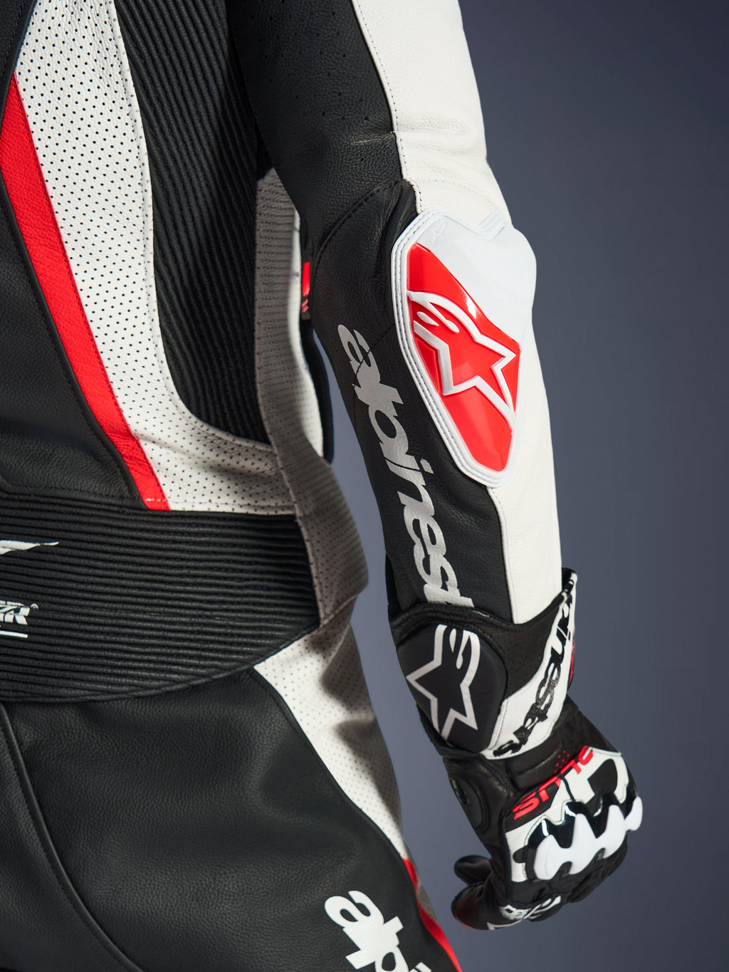 Primo piano della tuta in pelle 2 pezzi Alpinestars Stella GP-R7 da donna, nero, bianco e rosso fluo, con lo slider gomito GP DFS RR caratterizzato dal logo a stella rosso, scritta Alpinestars bianca sull'avambraccio, pelle traforata e pannelli a fisarmonica.