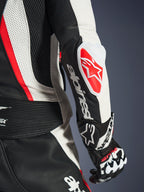 Primo piano della tuta in pelle 2 pezzi Alpinestars Stella GP-R7 da donna, nero, bianco e rosso fluo, con lo slider gomito GP DFS RR caratterizzato dal logo a stella rosso, scritta Alpinestars bianca sull'avambraccio, pelle traforata e pannelli a fisarmonica.
