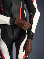 Tuta in pelle due pezzi Alpinestars Stella GP-R7 da donna, nero, bianco e rosso fluo, primo piano del pilota che regola la cerniera della manica, con pannelli in pelle traforata e marchio Tech-Air, abbigliamento professionale per competizioni motociclistiche