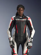 Modella che indossa la tuta in pelle 2 pezzi Alpinestars Stella GP-R7 nei colori nero, bianco e rosso fluo, con pannelli in pelle traforata e guanti GP Pro coordinati, anatomicamente ottimizzata per le motocicliste.