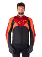 Giacca Alpinestars T-Jaws V4 Waterproof, giacca da moto sportiva in tessuto, nero con accenti rosso fluo e rosso scuro, indossata da un modello con guanti coordinati, abbigliamento tecnico con logo a stella sul petto