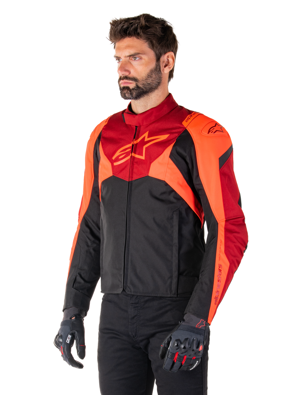 Giacca Alpinestars T-Jaws V4 Waterproof, nero, rosso fluo e rosso scuro, indossata da un modello uomo con pantaloni neri e guanti da moto, silhouette sportiva aggressiva con logo Alpinestars sul petto, vista a tre quarti