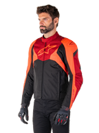 Giacca Alpinestars T-Jaws V4 Waterproof, nero, rosso fluo e rosso scuro, indossata da un modello uomo con pantaloni neri e guanti da moto, silhouette sportiva aggressiva con logo Alpinestars sul petto, vista a tre quarti