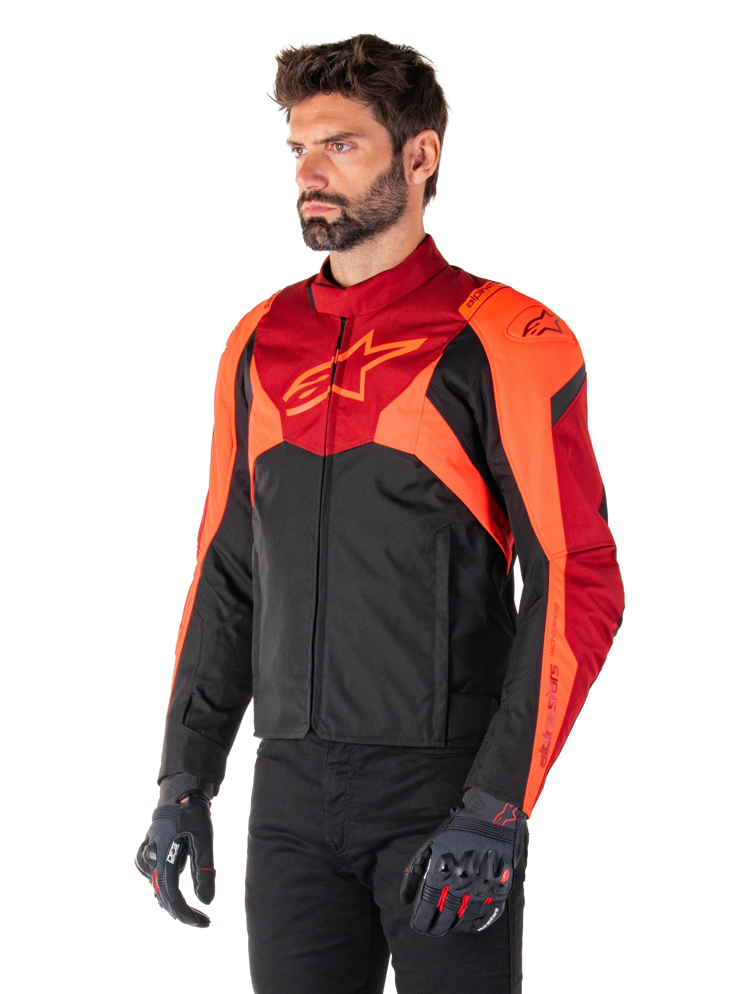Giacca Alpinestars T-Jaws V4 Waterproof, nero, rosso fluo e rosso scuro, indossata da un modello uomo con pantaloni neri e guanti da moto, silhouette sportiva aggressiva con logo Alpinestars sul petto, vista a tre quarti