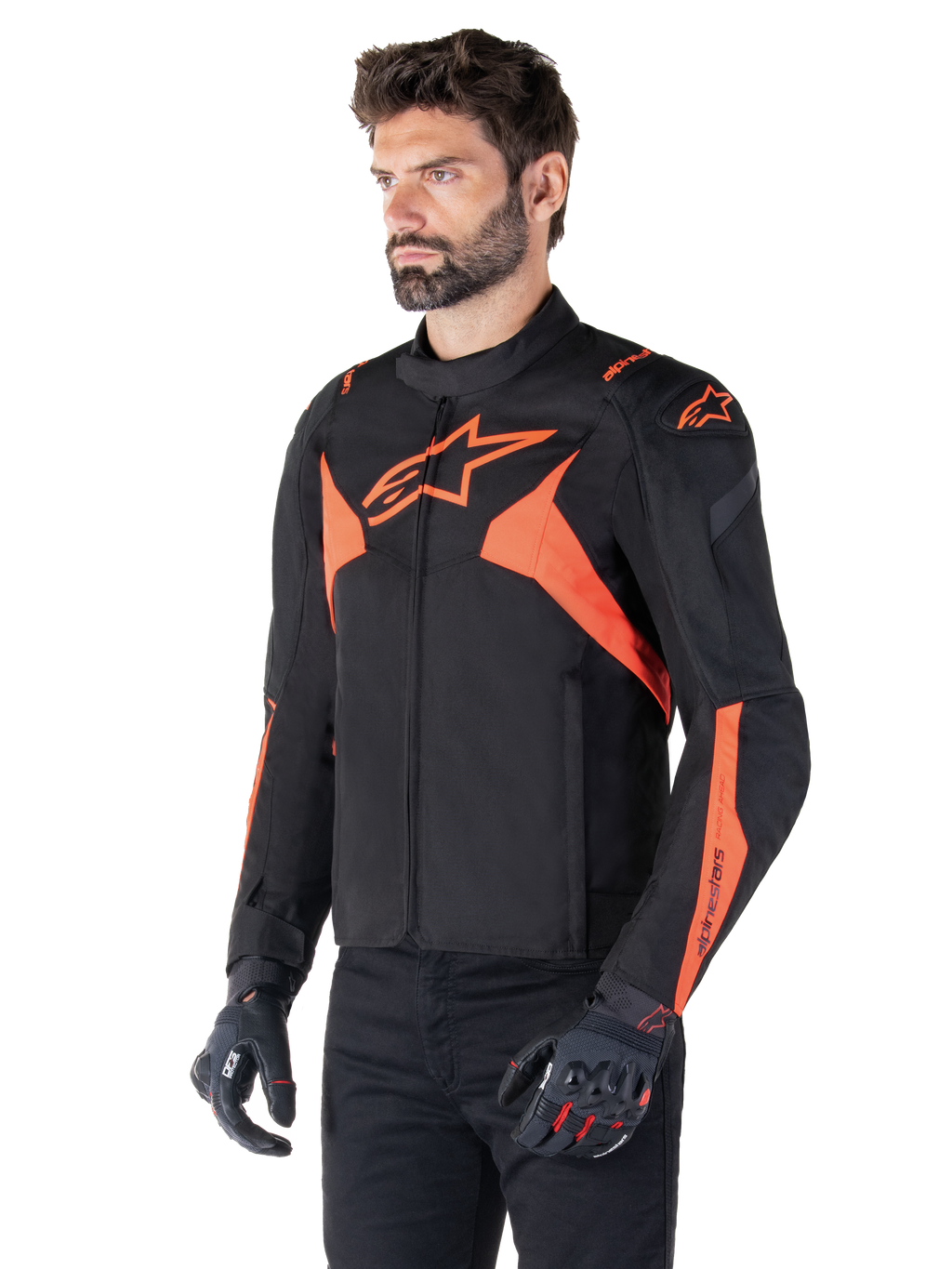 Giacca impermeabile Alpinestars T-Jaws V4, nero e rosso fluo, giacca da moto sportiva indossata da un modello, con loghi a stella arancioni in evidenza sul petto e sulle spalle, abbinata a guanti e pantaloni neri