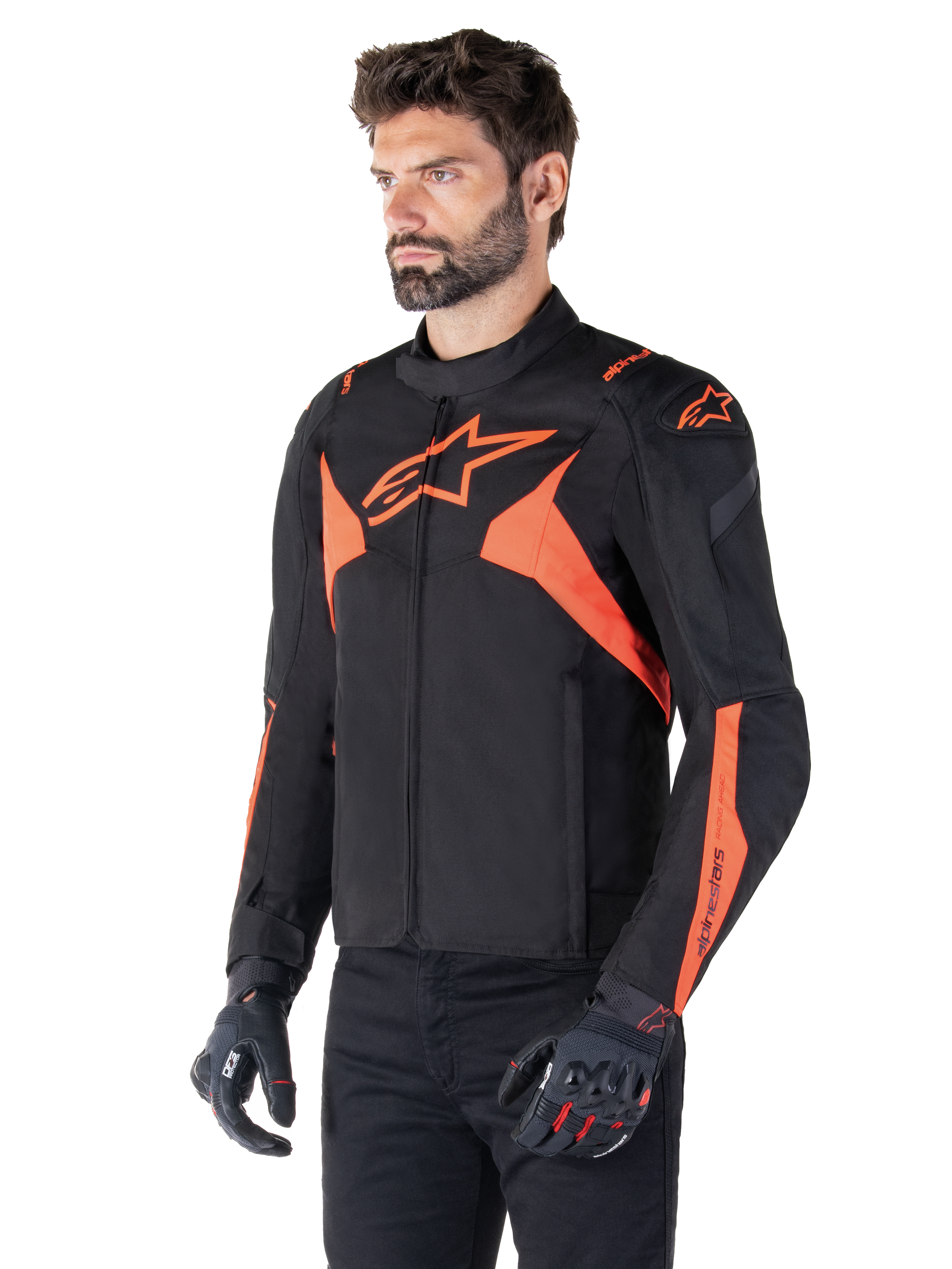 Giacca impermeabile Alpinestars T-Jaws V4, nero e rosso fluo, giacca da moto sportiva indossata da un modello, con loghi a stella arancioni in evidenza sul petto e sulle spalle, abbinata a guanti e pantaloni neri