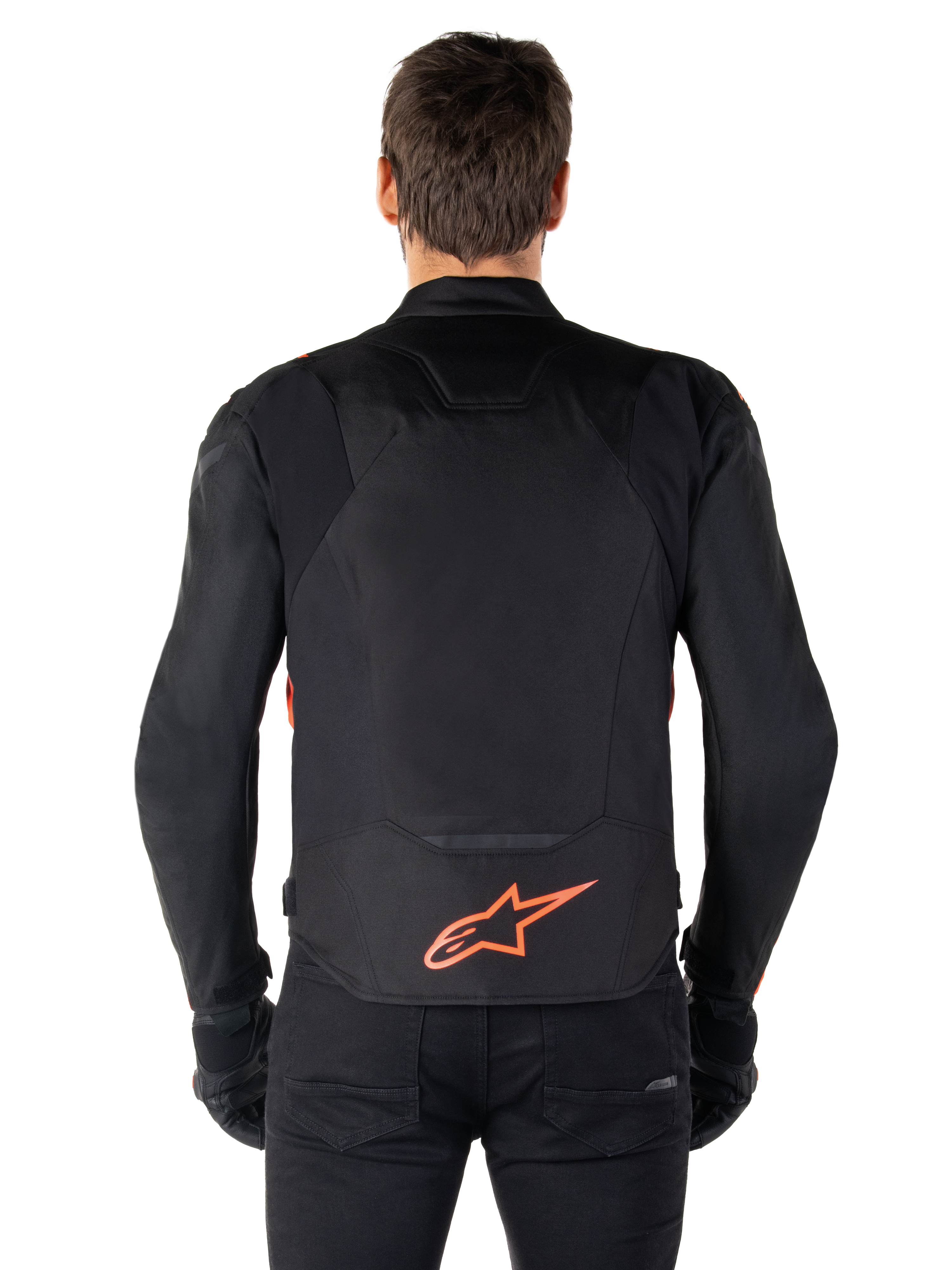 Giacca impermeabile Alpinestars T-Jaws V4, vista posteriore, nero con rosso fluo, con logo Alpinestars rosso sulla parte bassa della schiena, struttura in tessuto tecnico, indossata con pantaloni e guanti neri per un look da guida sportiva completo