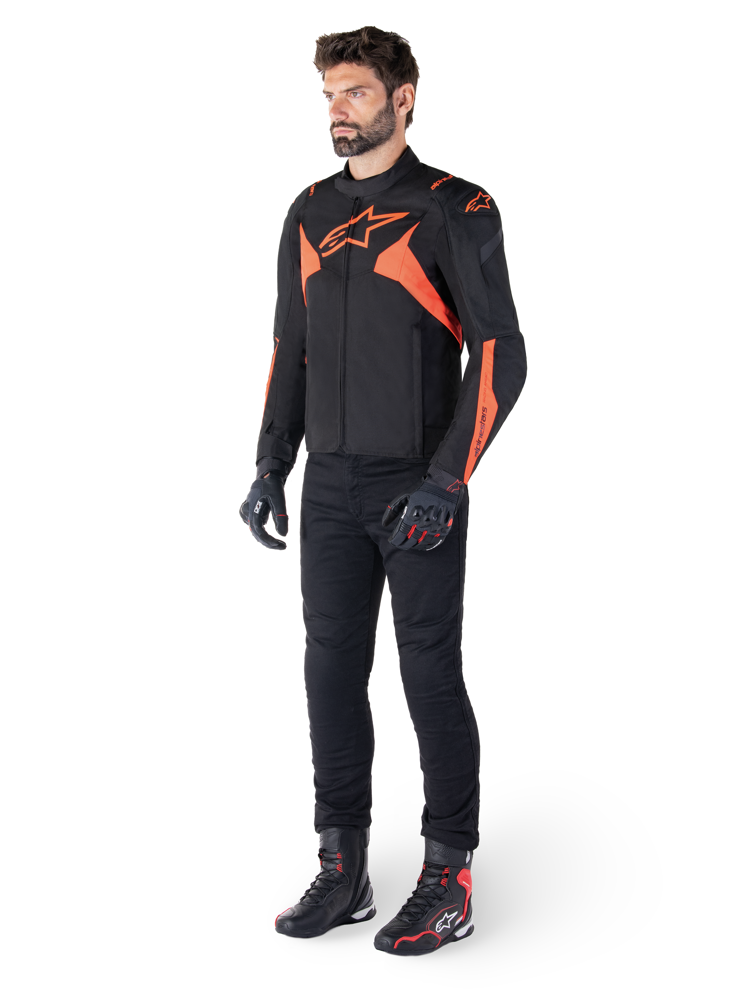 Giacca Alpinestars T-Jaws V4 Waterproof, nero e rosso fluo, indossata da un modello con pantaloni, guanti e stivali neri, con vivaci dettagli arancioni e il logo Alpinestars, design sportivo per la guida in moto